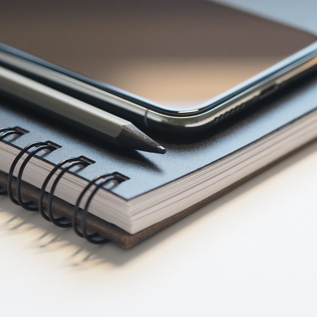 closeup photo of black smartphone near black and grey pencil on black spiral notebook